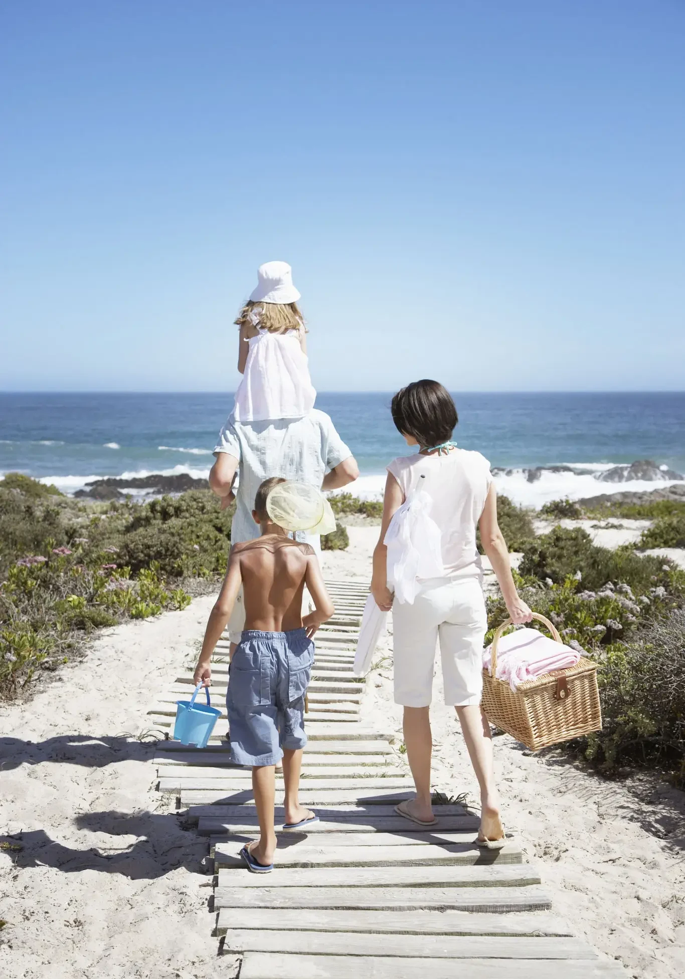 Family walking on boardwalk towards ocean beach.
